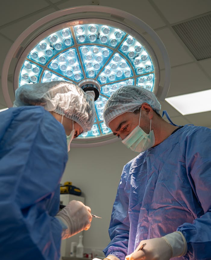 Two surgeons in sterile attire perform a surgical procedure under bright lights in an operating room.